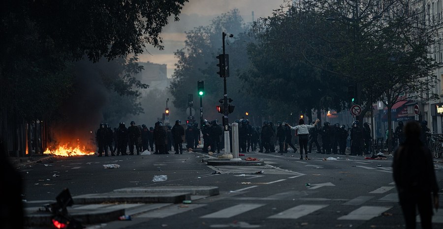 Police hold a line across a Paris street as fires burn during unrest in October 2026.